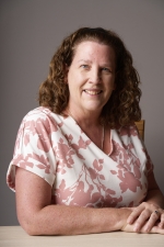 Professional headshot of Kathy Campbell wearing a pink and white shirt in front of a grey background..
