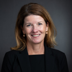 Woman smiling with shoulder length hair, wearing a black blazer and black blouse
