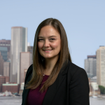 Woman with long brown hair wearing a black blazer and a purple blouse