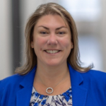 Woman smiling with shoulder length brown hair wearing a blue blazer and colorful blouse