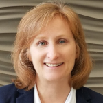 Woman smiling with shoulder length red hair in a navy blazer and white blouse