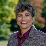 Woman smiling with short gray hair, wearing a plaid blazer and purple blouse