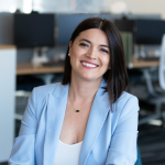 Headshot of Selma Mandzo-Preldzic. Woman smiling with dark shoulder length hair in a blue blazer and white blouse