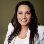 Headshot of smiling woman with dark brown hair in white blazer, white blouse, and pearl necklace