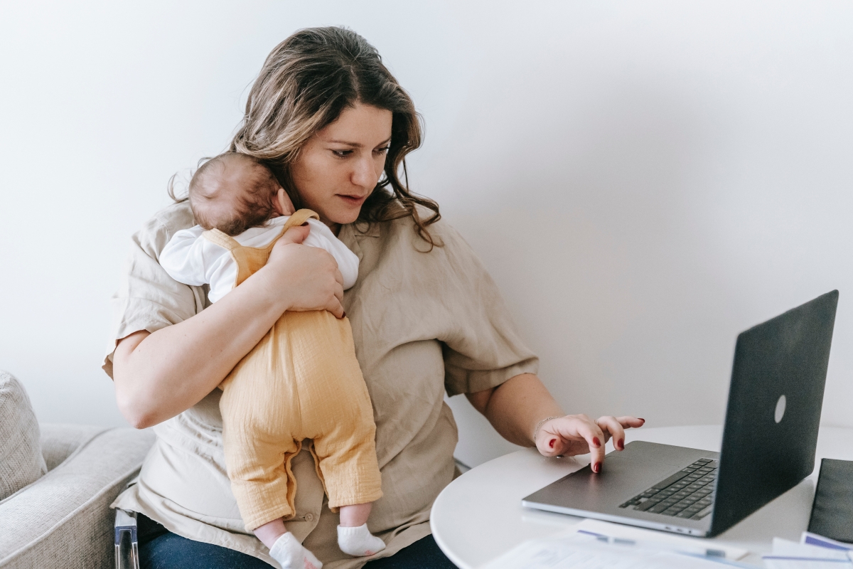 Working mother typing on laptop holding baby