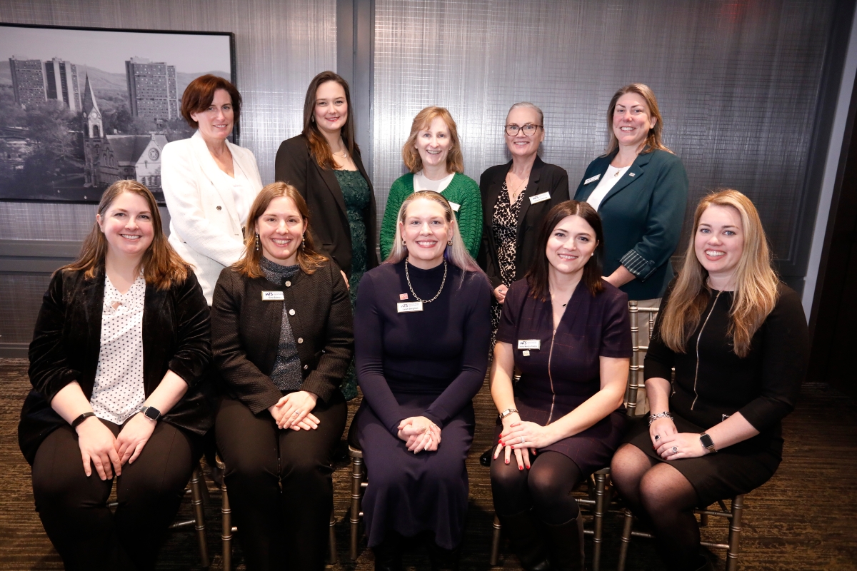 Five women standing and five women sitting smiling in a dark room.