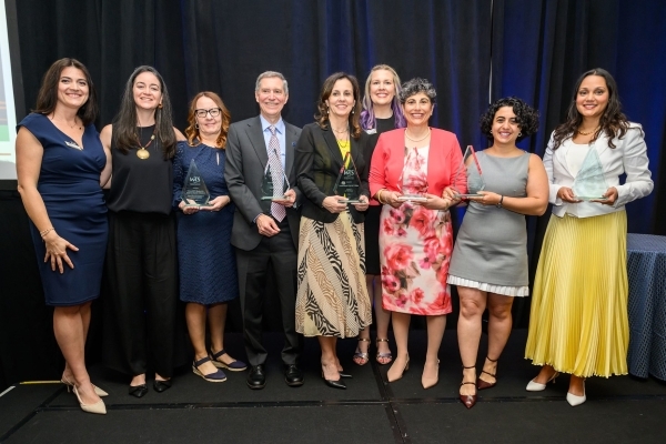 Eight women and one man in professional attire smiling holding awards