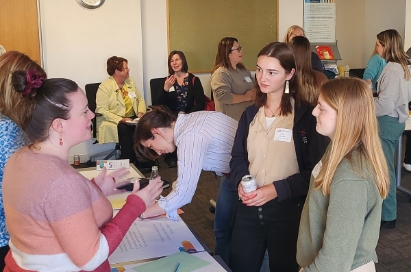 Room filled with people, foreground has three women in a discussion