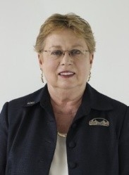 The headshot shows a person with short, light‑colored hair wearing a dark collared shirt, posed against a plain light background.