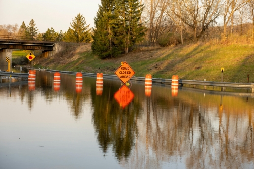 Traffic cones and signs reflected in the water of a flooded street