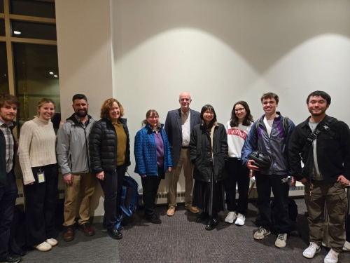 A small group of Northeastern students and AECOM presenters are standing in front of a white wall outside the lecture hall. In the middle is the AECOM presenter, Roger, and the WTS NEU president, Xinyi