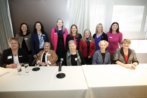 Group of women posing for the camera including the event speakers sitting in a row and the WTS leadership standing behind them.