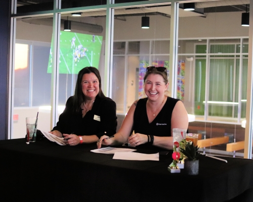 Two women sit behind a check-in table