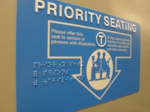 Priority seating sign for the MBTA with white lettering and braille