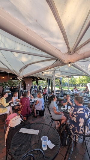 Candid photo of people sitting at tables under umbrellas at an outdoor patio.