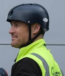 Smiling profile of a man in a black helmet, high visibility safety vest, and a black long-sleeved shirt.