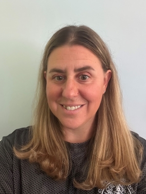 Smiling woman with long blonde hair in gray shirt, in front of white background.